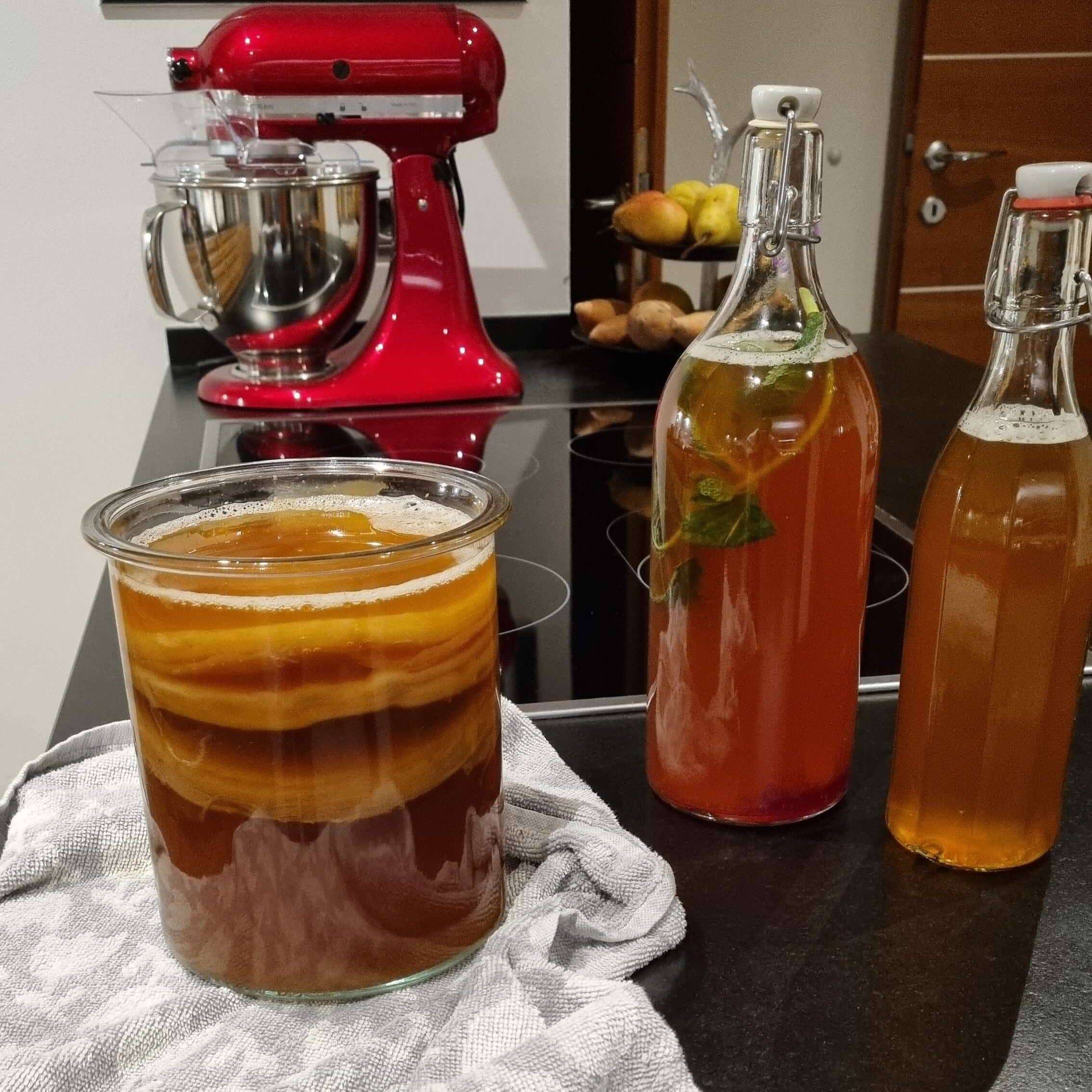 Homemade kombucha in flip top bottles ready for second fermentation and jar of freshly brewed tea with kombucha scoby inside ready for first fermentation
