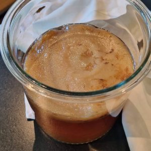 Kombucha SCOBY with yeast strands from above floating on surface of first fermentation in glass jar